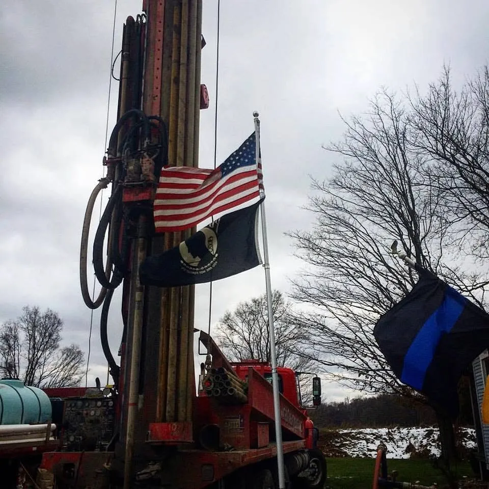 A Wahlfield drill rig under the flag on a clear day.