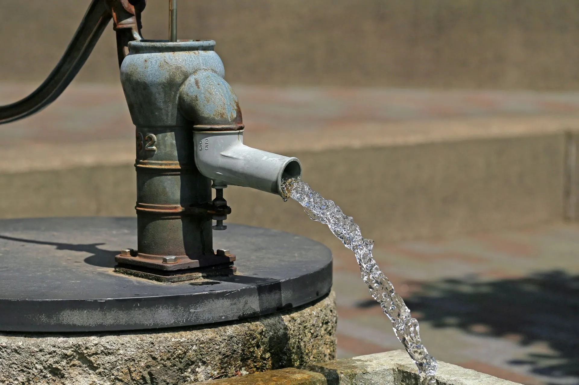 Cast-iron hand pump discharging water at an old well head