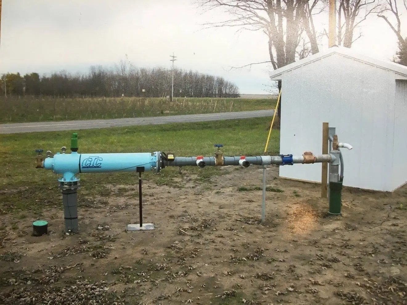 A wellhead and pitless adapter beside an outbuilding.